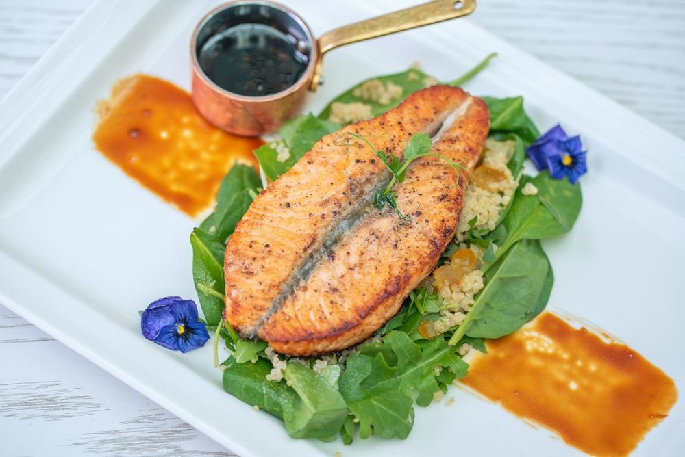 Pavé de saumon poêlé, quinoa, roquette et fleurs comestibles — plat traiteur dressé en gastronomie